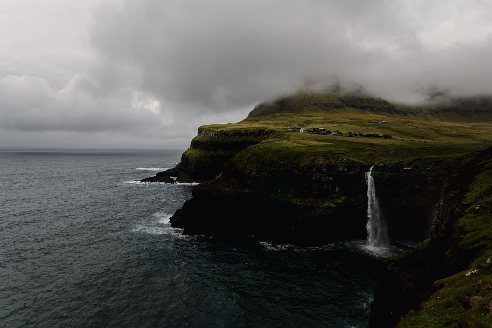 A waterfall falling of a cliff into a the ocean on the Faroe Islands captured by landscape photographer Chris Zielecki