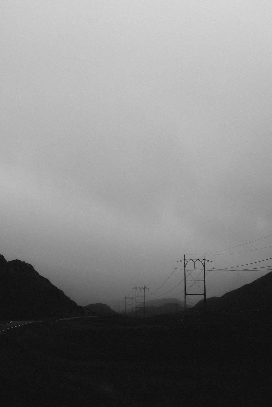 A series of power lines stretch across a dark, foggy landscape with hills on either side under a heavy, overcast sky in Norway.